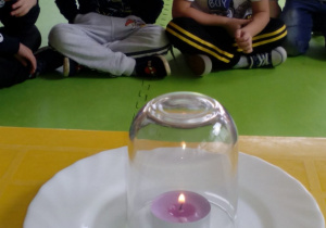 Dzieci obserwujące palący się podgrzewacz nakryty szklanką.